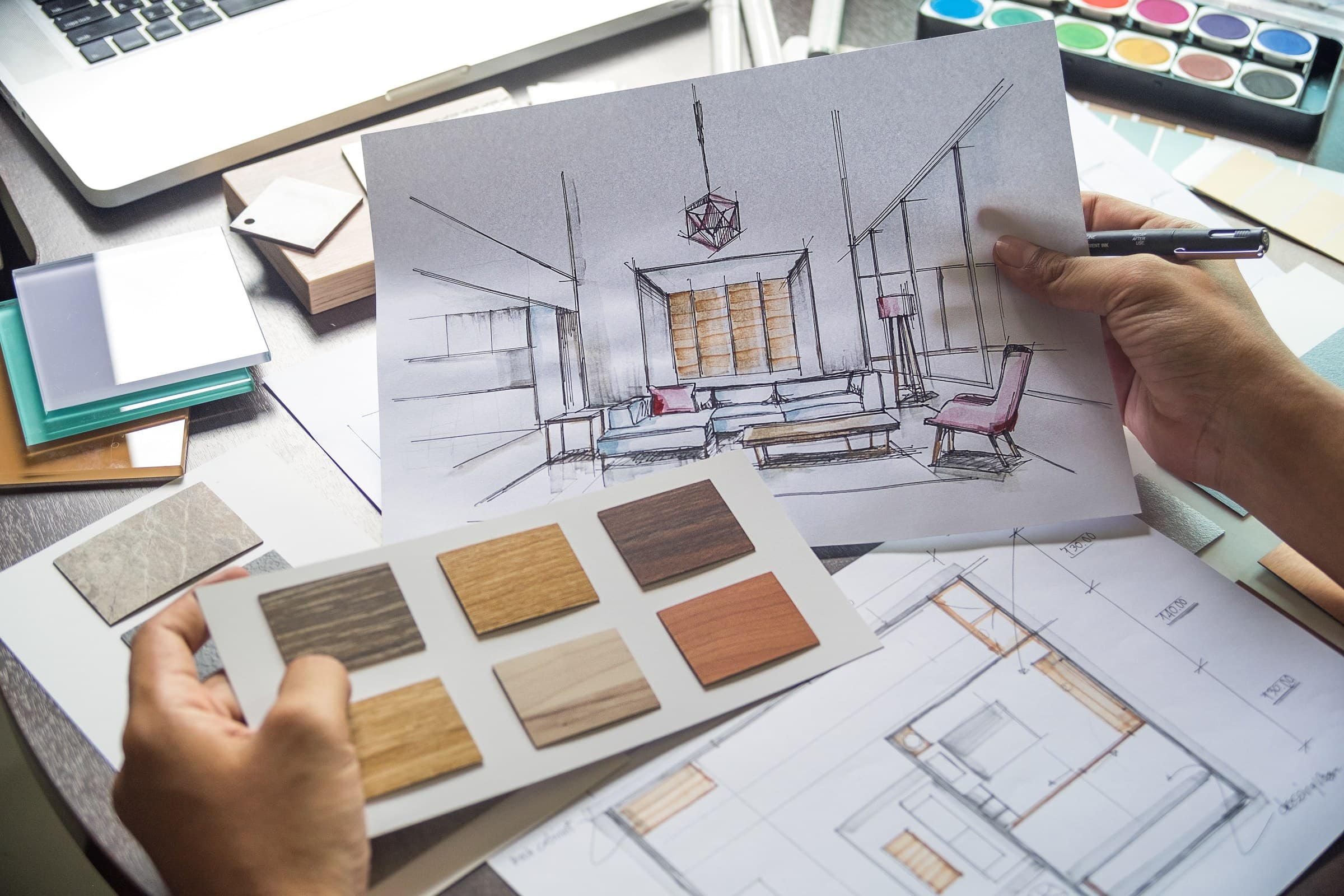 A designer holding a room sketch and wood finish samples over a floor plan