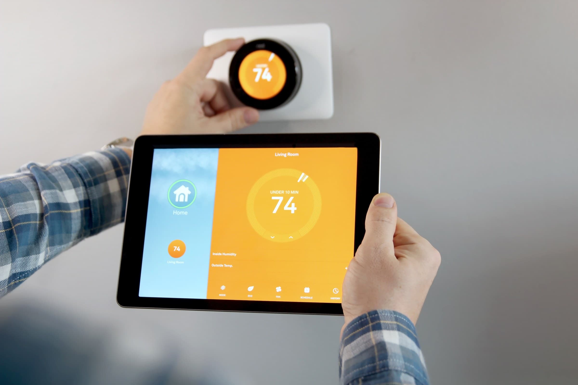 A homeowner adjusting a smart thermostat while checking the home's climate app on a tablet